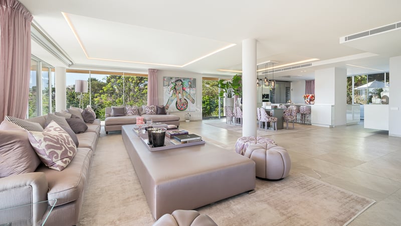 Vaste salon ouvert avec sol en marbre, accents roses, mobilier moderne et grandes baies vitrées sur le jardin.