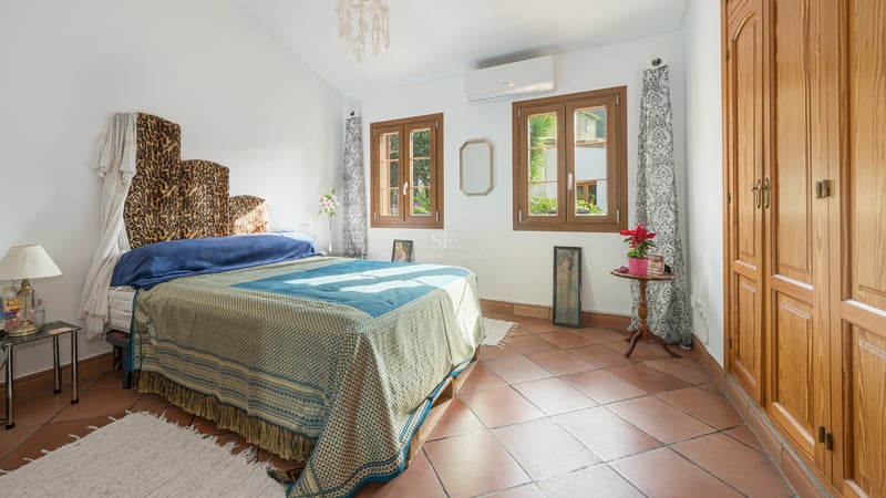 Chambre ensoleillée avec sol en terre cuite, grandes armoires en bois et fenêtres donnant sur la verdure.