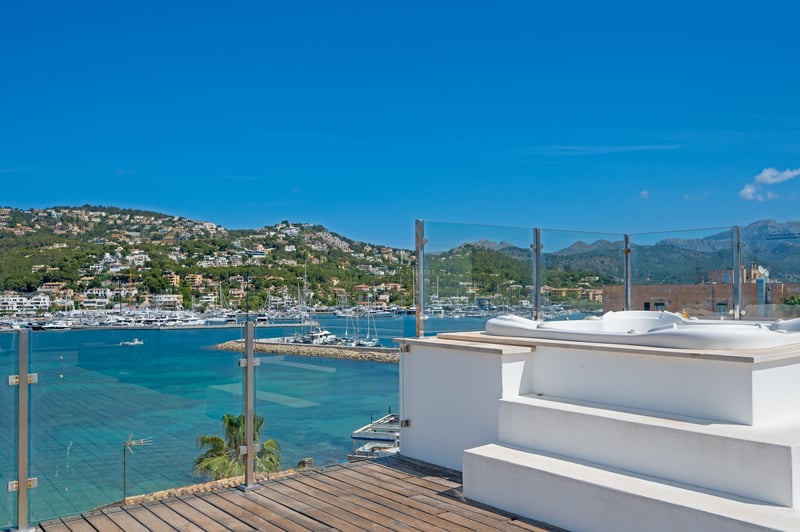 Terrasse sur le toit avec jacuzzi blanc, garde-corps en verre et vue panoramique sur le port de plaisance.