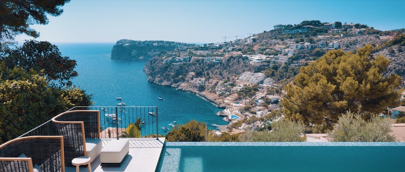 Terrasse de luxe avec piscine à débordement et fauteuils design surplombant une baie avec des yachts.