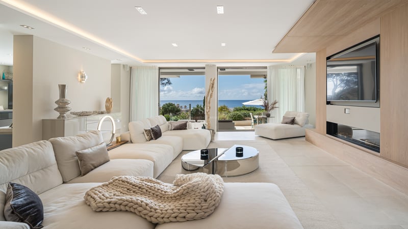Salon moderne avec canapés blancs, accents en chêne et grandes baies vitrées donnant sur la Méditerranée.
