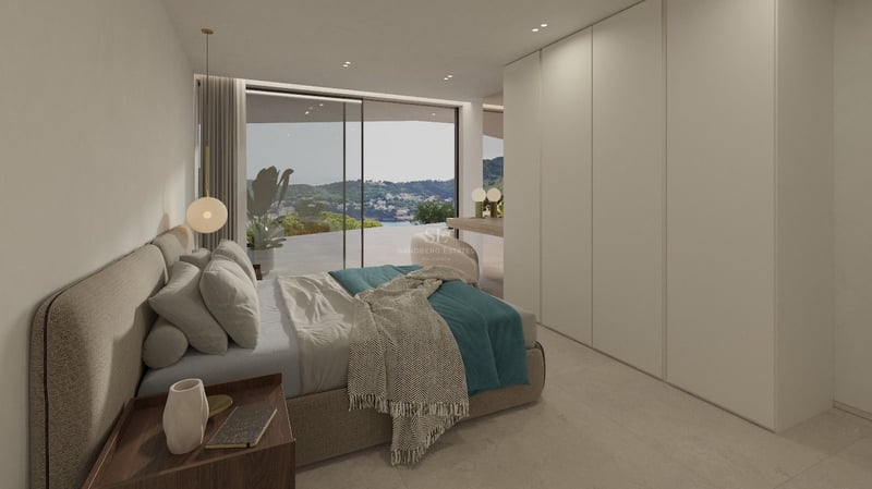 Chambre minimaliste avec lit rembourré, armoires encastrées et baies vitrées offrant une vue sur la mer et les montagnes.