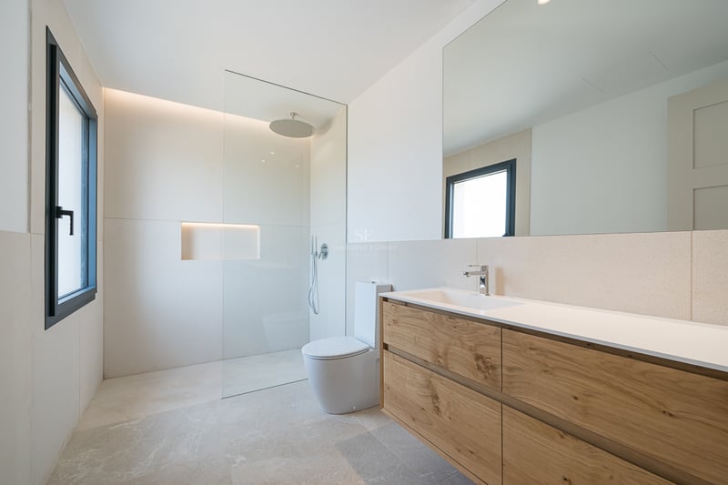Salle de bain lumineuse avec meuble en bois, grand miroir, douche à l'italienne et carrelage en pierre naturelle.
