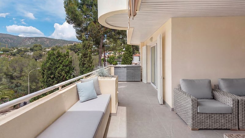 Terrasse couverte moderne avec meubles en rotin gris, banquette intégrée et vue sur les collines verdoyantes.