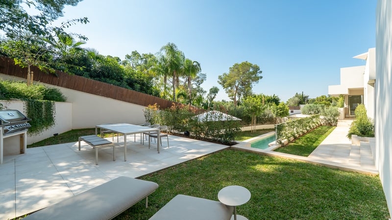 Terrasse moderne avec coin repas, barbecue et piscine entourée d'une végétation luxuriante et de palmiers.