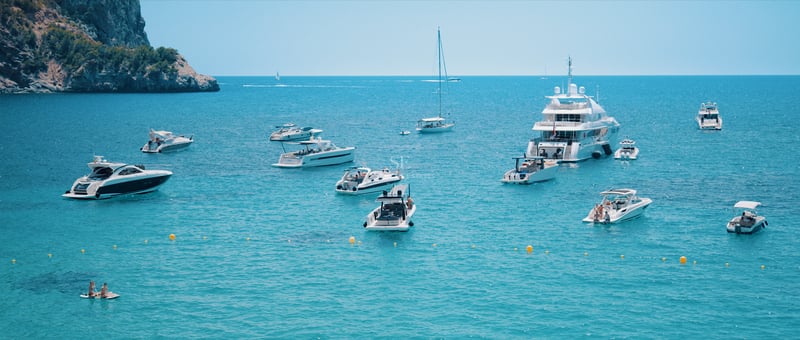 Plusieurs yachts de luxe et bateaux à moteur ancrés dans une baie aux eaux turquoise cristallines près de falaises.