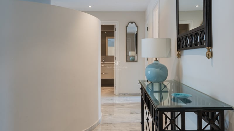 Entrée moderne avec mur incurvé, sols en marbre poli et console en verre avec lampe bleue.