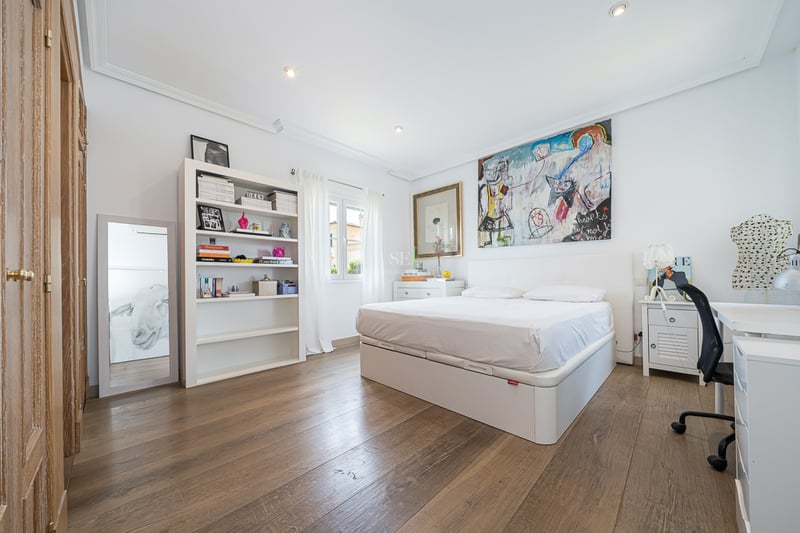 Chambre lumineuse avec murs blancs, parquet en bois, lit double, bibliothèque blanche et bureau.