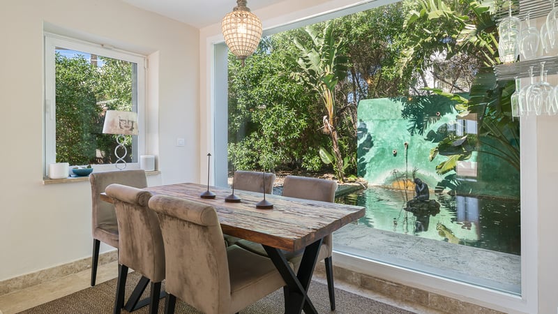 Salle à manger contemporaine avec table en bois rustique donnant sur un jardin avec bassin d'eau.