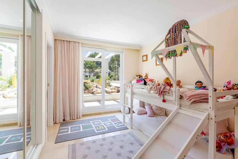 Chambre d'enfant avec lits superposés blancs et toboggan, sol en marbre et baies vitrées ouvrant sur le jardin.