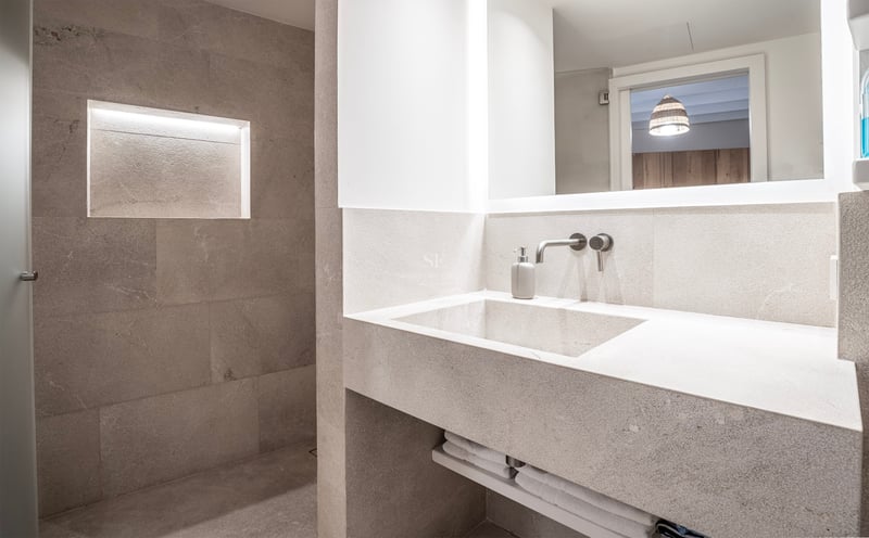 Salle de bain moderne avec lavabo en pierre intégré, miroir rétroéclairé et douche avec niche lumineuse.
