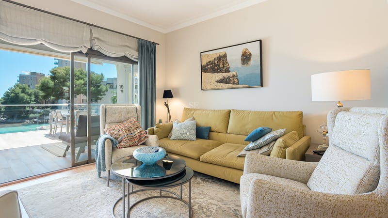 Salon lumineux avec canapé moutarde, fauteuils à motifs et baies vitrées ouvrant sur une terrasse ensoleillée.