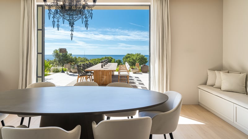 Salle à manger avec table en bois sombre s'ouvrant sur une terrasse ensoleillée avec vue sur la Méditerranée.