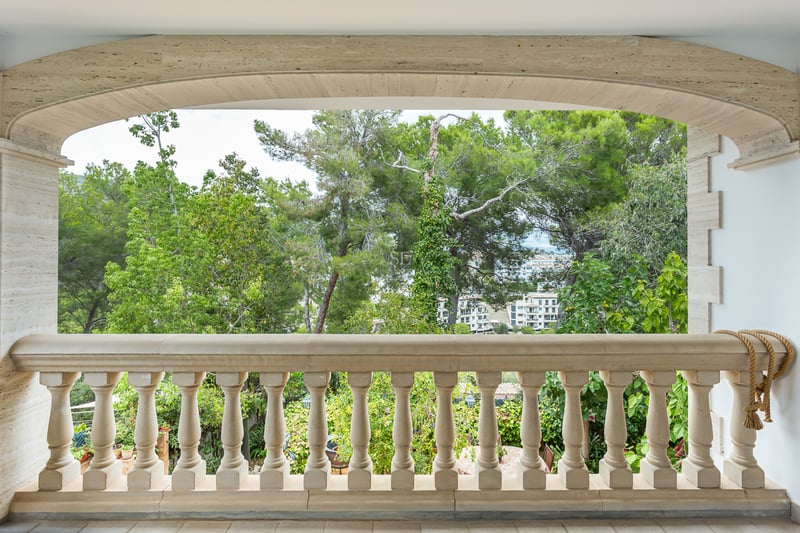 Balustrade en pierre beige sous une arche en pierre surplombant des arbres verts et des bâtiments au loin.