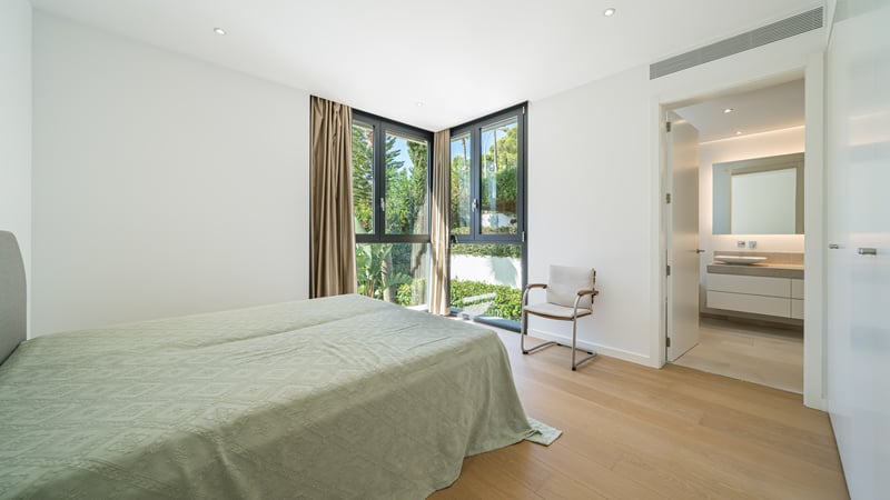 Chambre de maître lumineuse avec parquet, fenêtres d'angle et salle de bain moderne attenante.
