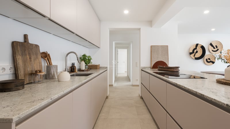 Cuisine moderne avec des placards beiges, des plans de travail en pierre et une vue sur un couloir blanc.