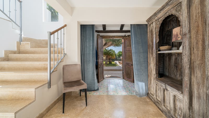 Hall d'entrée avec escalier en pierre, armoire en bois ancienne et portes ouvertes sur le jardin.