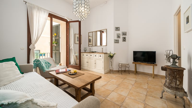 Salon spacieux avec sol en terre cuite, table basse en bois et grandes portes ouvrant sur un balcon.