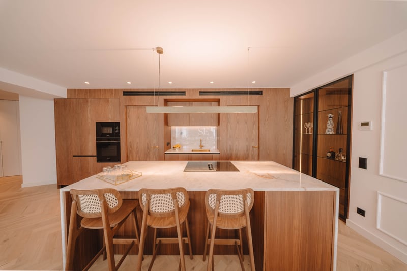 Cuisine moderne avec îlot en marbre blanc, tabourets en bois et armoires en bois sur mesure.
