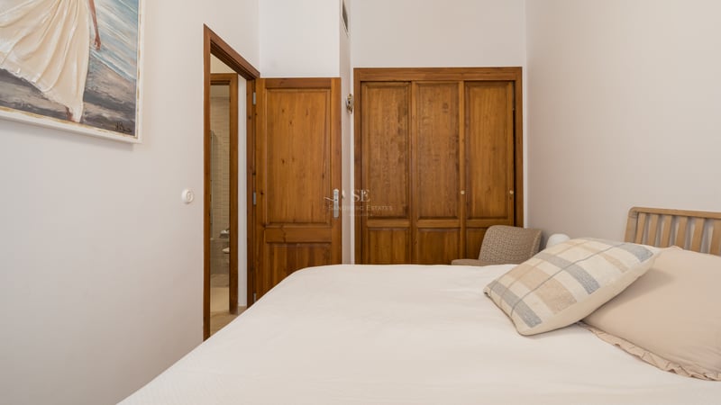 Chambre avec placards en bois massif, lit aux tons neutres et vue sur la salle de bain attenante.