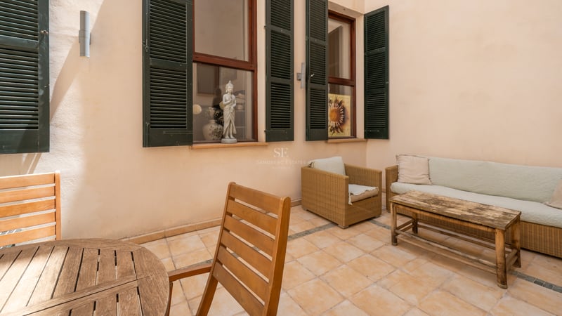 Terrasse privée avec carrelage en terre cuite, volets majorquins verts et mobilier en bois et rotin.