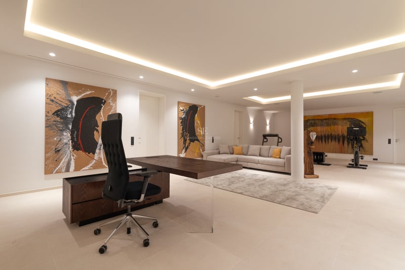 Bureau moderne spacieux avec bureau en bois sombre, canapé gris, art abstrait et coin fitness en arrière-plan.