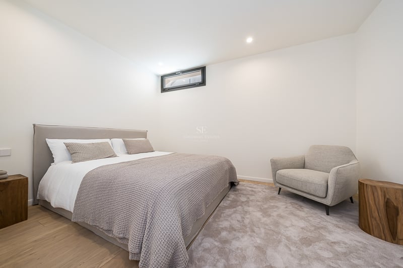 Modernes Schlafzimmer mit Doppelbett, grauem Sessel, Nachttischen aus Naturholz und hellem Eichenparkett.