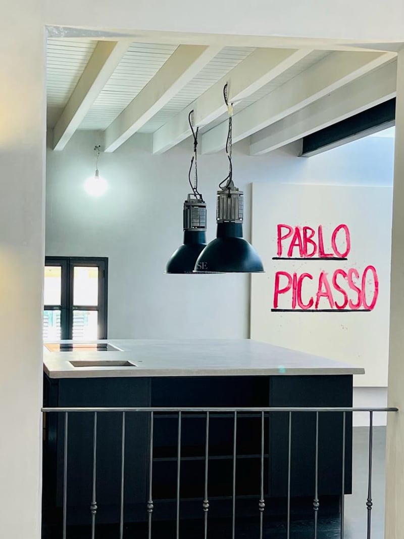 Îlot de cuisine moderne avec plan de travail gris, suspensions industrielles noires et plafond à poutres blanches.