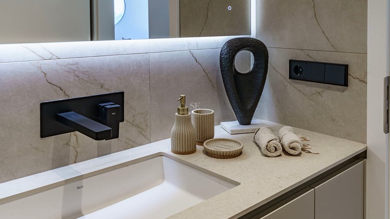 Gros plan d'un lavabo blanc avec robinet noir mat, mur en marbre beige et accessoires design.