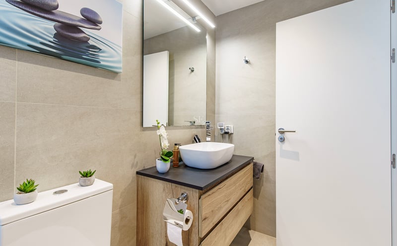 Salle de bain moderne avec vasque à poser, meuble en bois, murs carrelés beige et miroir avec éclairage LED.