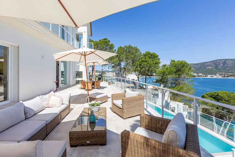 Grande terrasse en pierre blanche avec mobilier en rotin, garde-corps en verre et vue sur la mer et les montagnes.