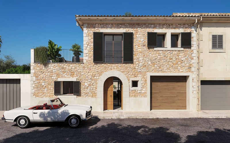Maison de village en pierre avec porte voûtée, volets sombres et cabriolet Mercedes classique blanc stationné devant.