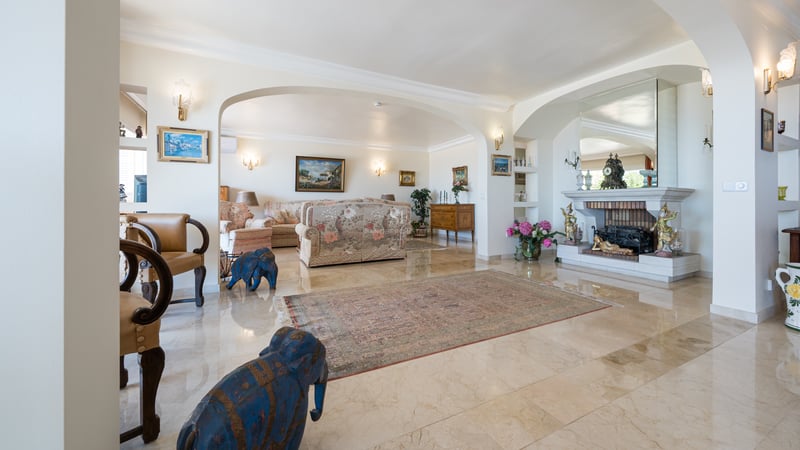 Grand salon avec sols en marbre crème poli, cheminée en pierre et ouvertures voûtées.