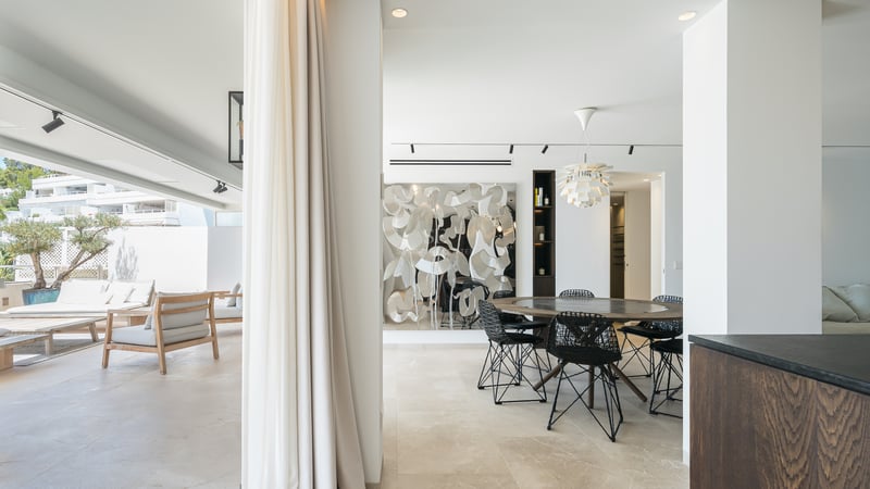 Salle à manger moderne avec table ronde en bois s'ouvrant sur une terrasse ensoleillée avec mobilier de salon.