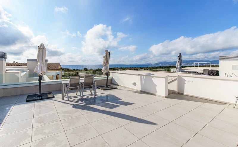 Grande terrasse moderne avec carrelage blanc, garde-corps en verre et coin repas avec vue sur la mer bleue.