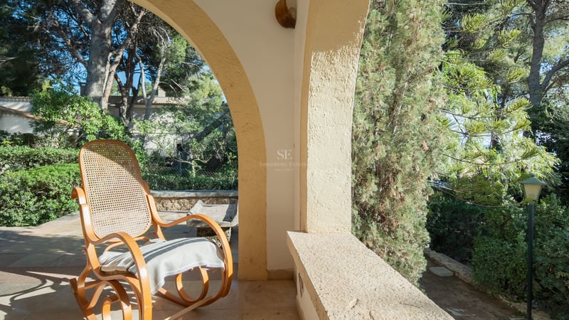 Un fauteuil à bascule classique sur une terrasse voûtée en pierre surplombant un jardin verdoyant.