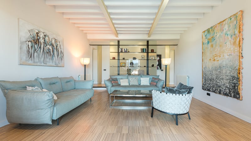 Grand salon avec canapés bleu clair, plafond à poutres blanches, parquet et grandes peintures abstraites.