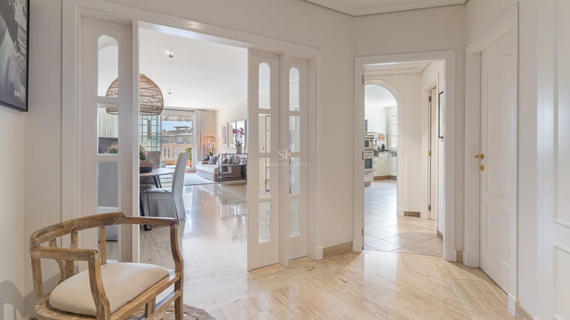 Vue depuis un hall en marbre vers un salon et une cuisine, avec des portes coulissantes blanches et du bois naturel.