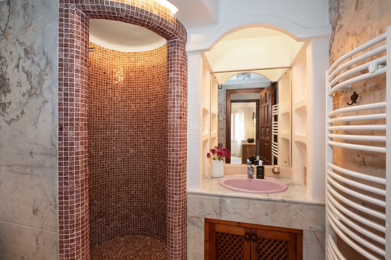 Douche à l'italienne courbe en mosaïque rougeâtre à côté d'un meuble vasque en marbre avec un évier rose.