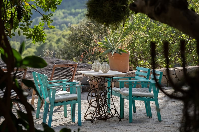 Table en marbre vintage et chaises en bois bleu canard sur un patio en pierre entouré de verdure méditerranéenne.