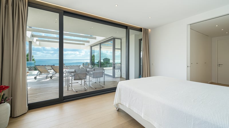 Chambre moderne avec lit blanc et grandes baies vitrées ouvrant sur une terrasse avec vue mer.
