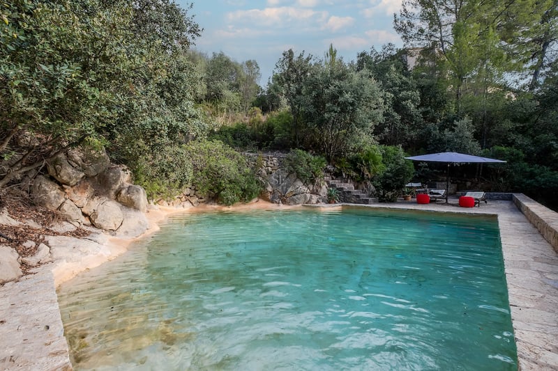 Piscine style lagon aux eaux turquoise avec bordures en pierre naturelle et coin détente ombragé.
