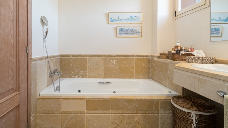 Baignoire d'hydromassage blanche entourée de marbre beige, robinetterie chromée et détails en bois.