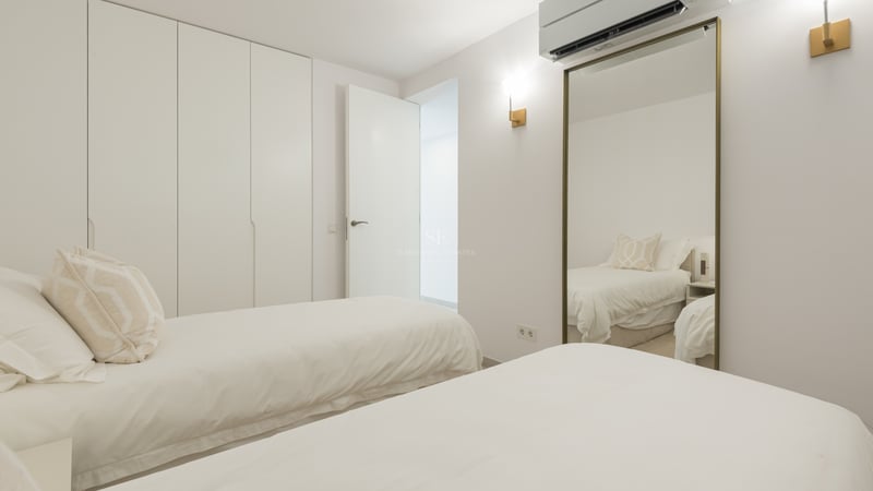 Chambre minimaliste lumineuse avec deux lits simples, de grandes armoires blanches et un miroir avec cadre doré.