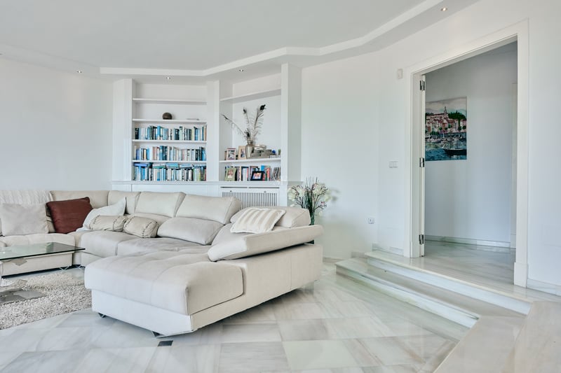 Salon contemporain avec sol en marbre blanc, grand canapé d'angle crème et bibliothèque intégrée blanche.