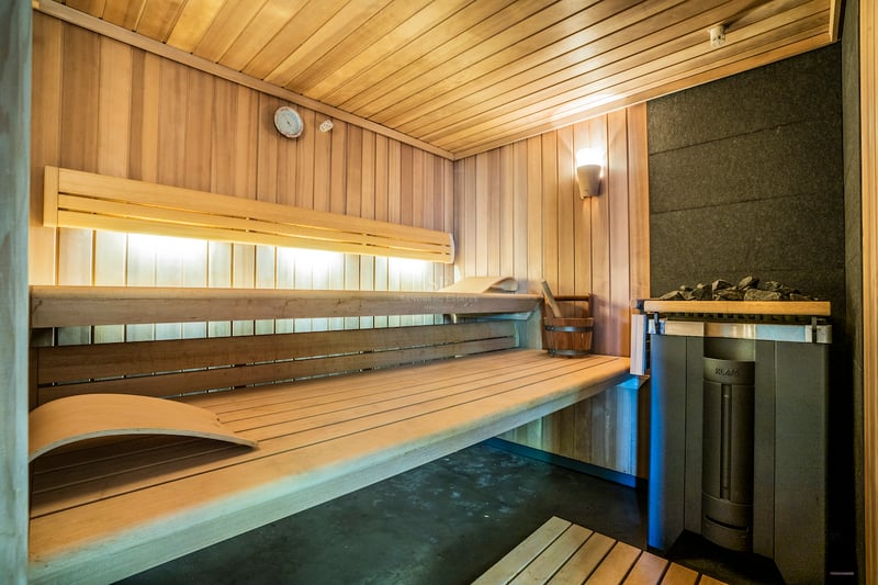 Intérieur d'un sauna moderne en bois avec bancs à plusieurs niveaux, éclairage d'ambiance et poêle KLAFS.
