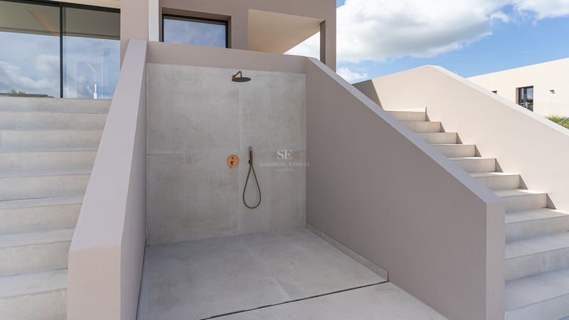 Douche extérieure minimaliste avec murs en microciment gris clair et robinetterie en laiton.