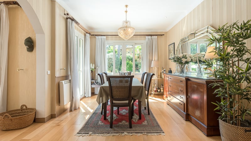 Salle à manger ensoleillée avec table en bois, lustre en cristal et grand buffet donnant sur l'extérieur.
