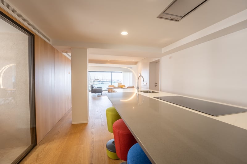 Îlot de cuisine avec tabourets colorés menant à un salon lumineux avec vue sur le port.