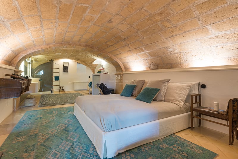 Bedroom featuring a low sandstone vaulted ceiling, white walls, and turquoise patterned rugs with a modern bed.